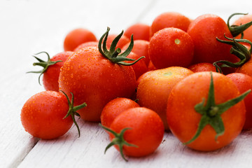 Mixed wet large and small tomatoes with stalks on white wood board.