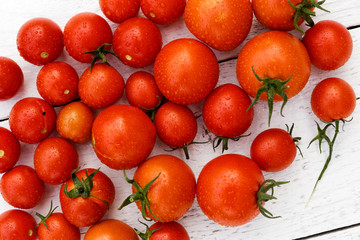 Many wet red  tomatoes with stalks on white wood board from above.