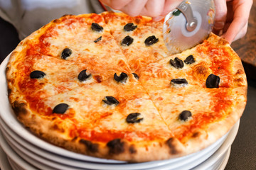 Cutting cheese pizza with pizza slicer.
