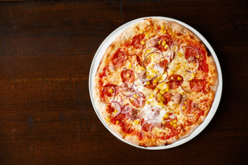 Salami and sweetcorn pizza isolated on dark brown table from above.