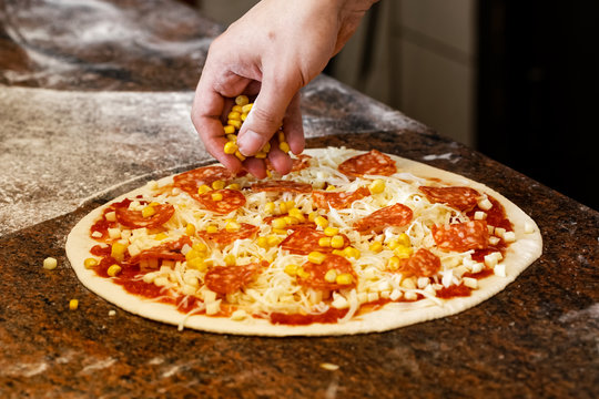 Cook's hands putting sweetcorn on tomato base pizza.