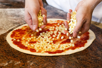 Cook's hands putting mozzarella cheese on tomato base pizza.