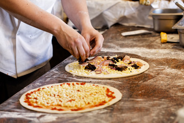 Cook putting toppings on two pizzas.