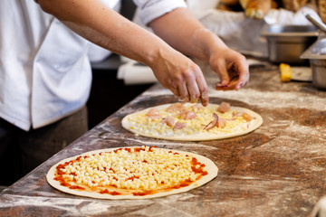 Cook putting toppings on two pizzas.
