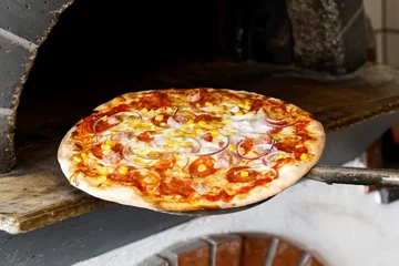 Foto op Plexiglas Baked salami pizza on metal paddle in front of wood oven. © Moving Moment