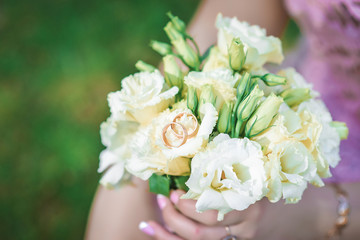 A wedding bouquet in the hands of a young bride with engagement rings on a bouquet. 