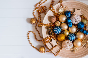 Beads, gold and blue balls. New Year composition in wooden plate.pine cones and Christmas tree decorations on wooden, white background. Copy space. Selective focus.Top view