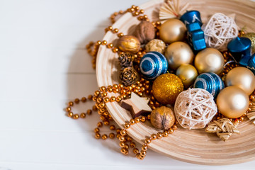 Beads, gold and blue balls. New Year composition in wooden plate.pine cones and Christmas tree decorations on wooden, white background. Copy space. Selective focus.Top view