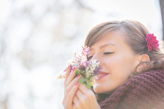 Cute young girl smelling nice bouquet of flowers in nature.