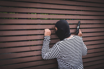 Robber hiding behind the wall, looking at victims and waiting to come nearest for stealing the...
