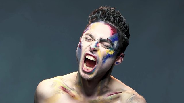 Angry young man screaming, slow-mo. Caucasian guy wearing artistic makeup. The beast inside.