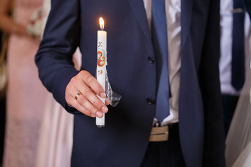 The groom in a blue suit and tie holding a white candle in church