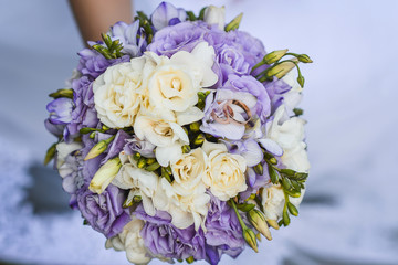 A gentle wedding bouquet in the hands of the bride on which two golden engagement rings of the groom and the bride lie on top.