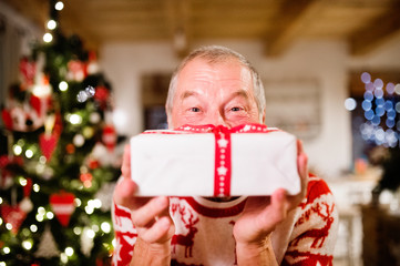 Obraz na płótnie Canvas Senior man in front of Christmas tree holding a gift.