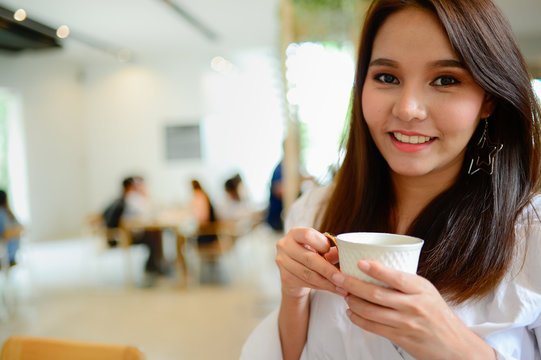 smile of beautiful woman and her hand holding a cup of coffee in blur background coffee shop