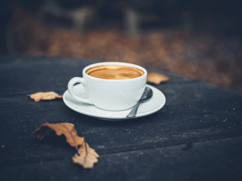 Cup of coffee on table with leaves in autumn