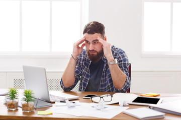 Young stressed businessman with laptop in modern white office