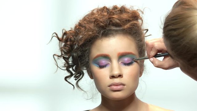 Makeup artist applying eyeshadow isolated. Young model on white background.