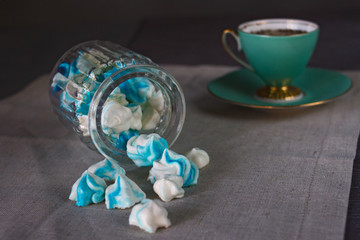 Appetizing sweet homemade blue and white marshmallows in a glass jar and a mug of tea on a canvas...
