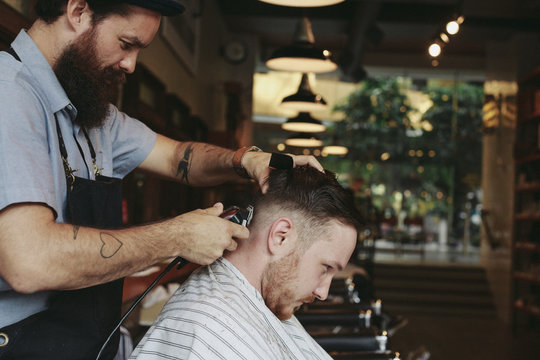 Stylish modern barber using clippers while giving man a classic haircut