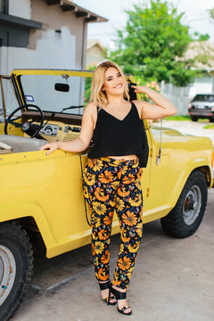 A young mixed ethnic woman in stylish clothes, posing in front of a yellow bronco outside.