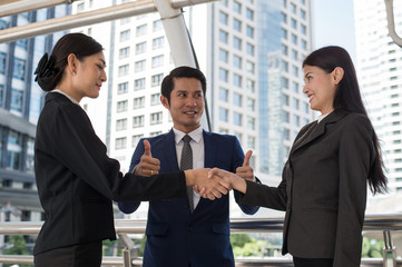 business man show thumb up and two business woman shaking hands for demonstrating their agreement to sign agreement or contract between their firms, companies, enterprises. success concept