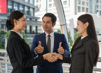 business man show thumb up and two business woman shaking hands and smile for demonstrating their agreement to sign agreement or contract between their firms, companies, enterprises. success concept