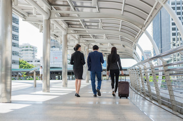 businessman and businesswoman walk together with mobile tablet and luggage on the public street, business travel