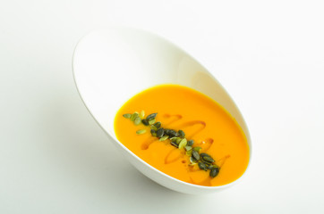 Pumpkin cream soup decorated pumpkin seeds in a bowl isolated on white background