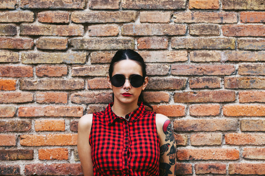 Young alternative woman standing in front a brick wall.