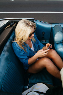 young teen female texting on mobile cell phone in back of convertible car in summer