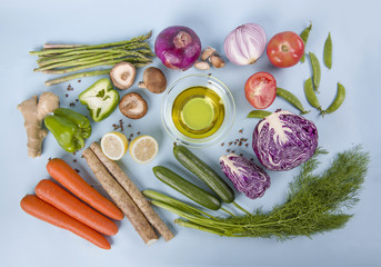 Collection of fresh vegetables and bowl of olive oil on blue background. Top view.