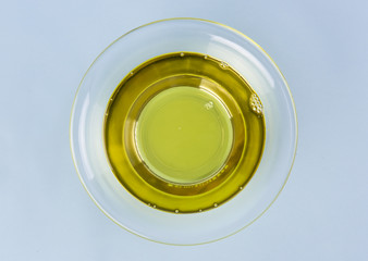 Olive oil in a glass bowl and on blue background.