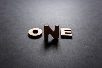 Word One of wooden letters on a dark texture with a black background with backlight. Lighting...