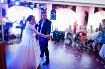 Beautiful wedding couple performing their first dance in the restaurant with different lights and bubbles and guests on the background.