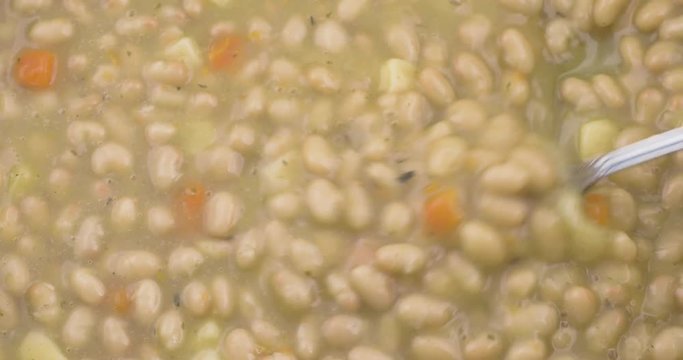 Close video of using a spoon to get a spoonful of hot bean soup from a pan.