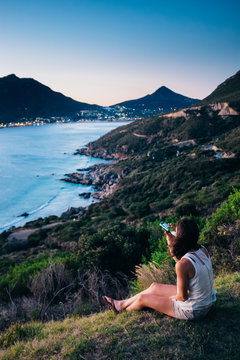 Woman sitting having a drink whilst enjoying dusk overlooking a beautiful coastal valley