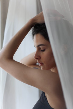 Woman in a black undershirt standing near the window