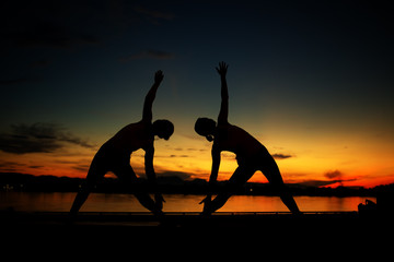 Silhouette young two women practicing yoga pose on the mekong riverside at sunrise.
