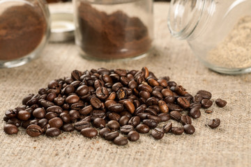 Pile of roasted coffee beans and glass jars with ground coffee