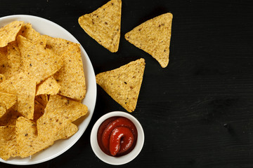 Nachos in a white plate with salsa sauce on a black table, top view