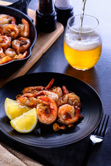 Skillet roasted jumbo shrimp on a black plate. Beer pouring into a glass.
