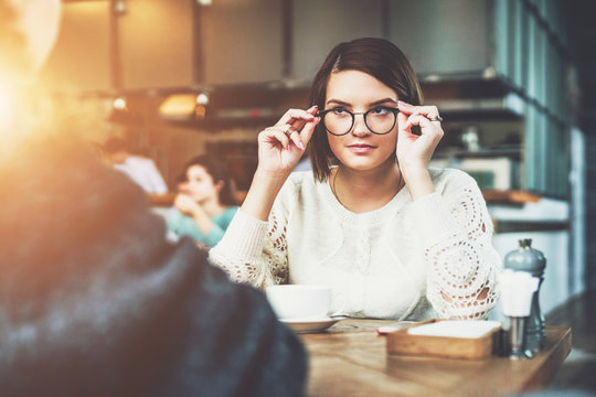 Business meeting. Portrait of a young business woman wearing glasses, sitting in cafe at table. Business lunch, break. Meeting friends. Colleagues have lunch together. Instagram filter. Film effect.