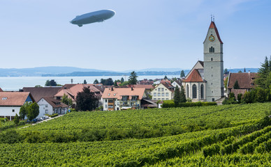 Zeppelin and Catholic Church St. Johann Baptist in Hagnau at Lake Constance with vitaceous in the foreground - Hagnau, Lake Constance, Baden-Wuerttemberg, Germany, Europe © karlo54