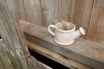 Dirty Watering Pot with Dried Plant on Wooden Shelf