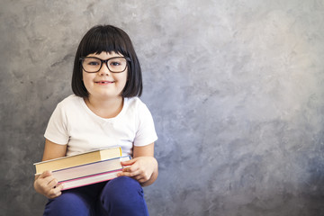 Cute black hair little girl with glasses holding books by the wall