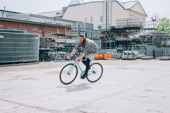 Hipster With Baseball Cap Riding Fixed Gear Bicycle on Industrial Plot