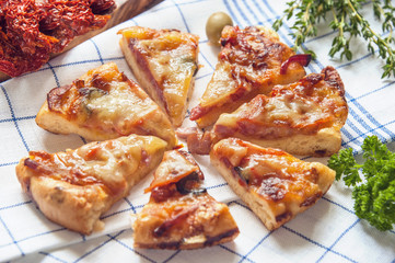 Round sausage pizza Margherita with pieces on a napkin with dried tomatoes and herb thyme and rosemary . Selective focus.