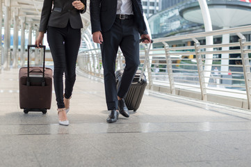business man and business woman walk together luggage on the public street, business travel