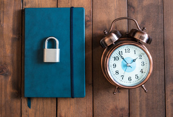 locked and key on Blue notebook on wooden background with vintage alarm clock.